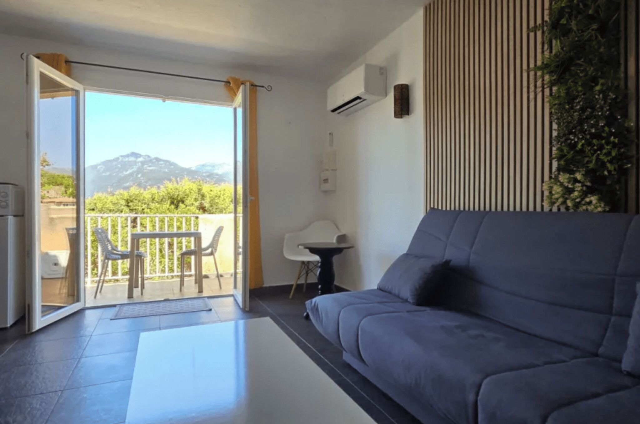 A modern living room with a sofa, a small table, and a balcony with a view of mountains.