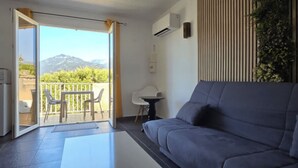 En moderne stue med sofa, et lille bord og en balkon med udsigt til bjerge.