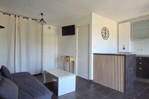 A modern living room with a sofa, a small table, a TV mounted on the wall, and a kitchen area with a counter and cabinets. - Dolce & Vita Studio D3 with ocean and pool views (Propriano)