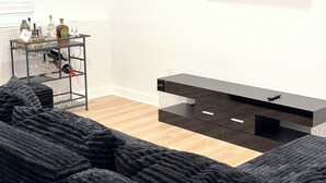 Una sala de estar moderna con un televisor de pantalla plana montado en la pared, un mueble de entretenimiento negro y un sofá grande de color oscuro.