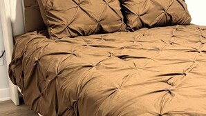 Una cama con cubierta acolchada marrón, una alfombra mullida y un radiador blanco.