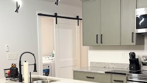 Una cocina moderna con una isla central, taburetes de bar, un cubo de basura de acero inoxidable y un microondas sobre la encimera.