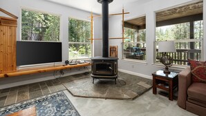 A living room with a stone fireplace, large windows, a TV, and a cozy seating area. - Candal Crest in Tamarack (Big Creek)