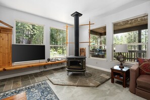 A living room with a stone fireplace, large windows, a TV, and a cozy seating area. - Candal Crest in Tamarack (Big Creek)