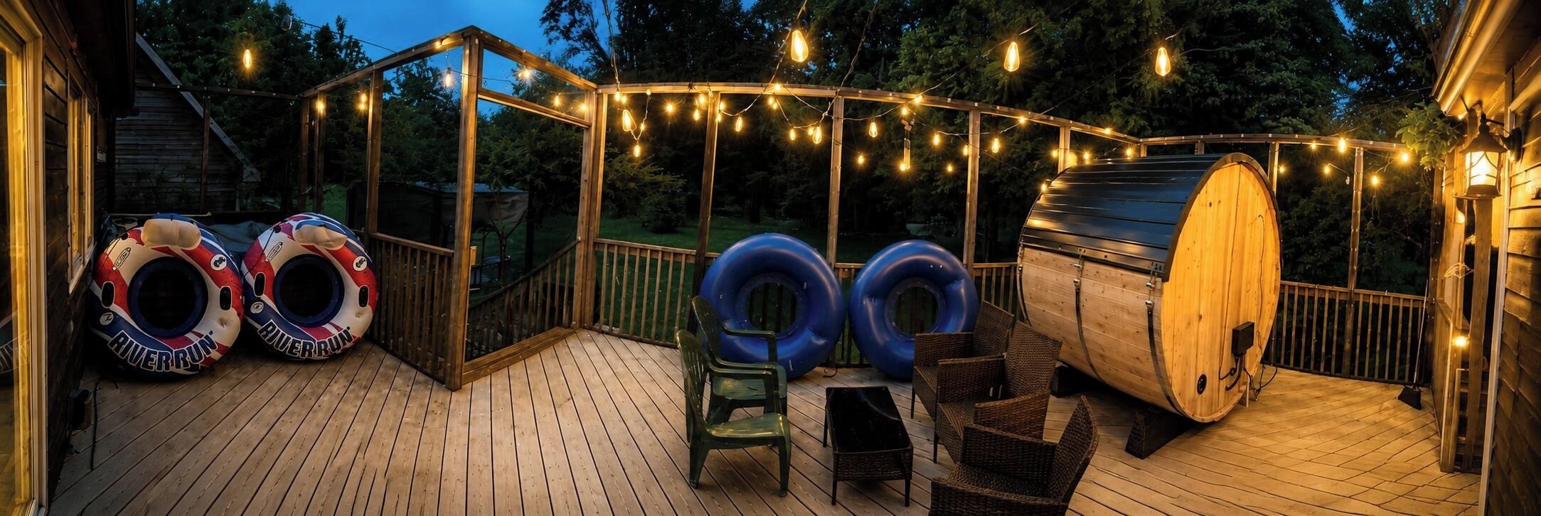 A wooden deck with a glass enclosure, inflatable rings, a barrel, and string lights.