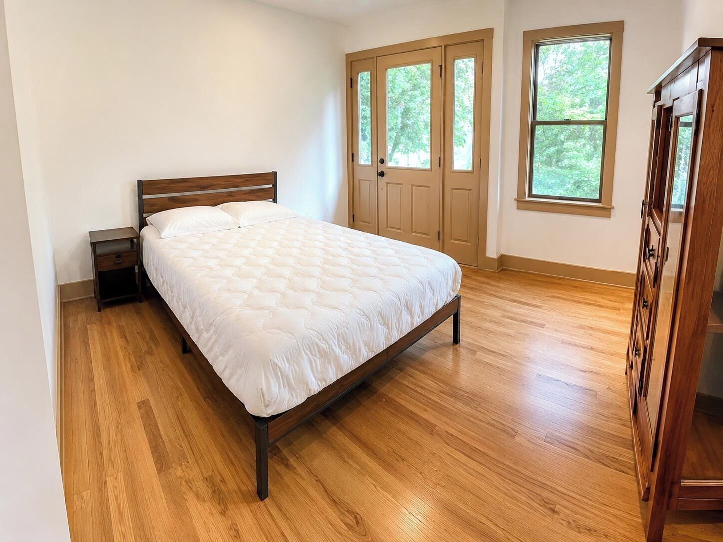 A bedroom with a wooden bed, a nightstand, a wardrobe, and a door with windows.