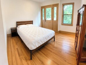 A bedroom with a wooden bed, a nightstand, a wardrobe, and a door with windows.