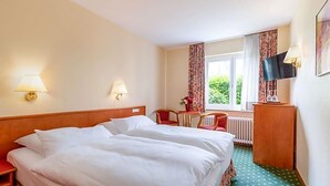 A hotel room with a double bed, two bedside lamps, a small table with a chair, a TV, and a window with curtains. - Alte Post (Krefeld)