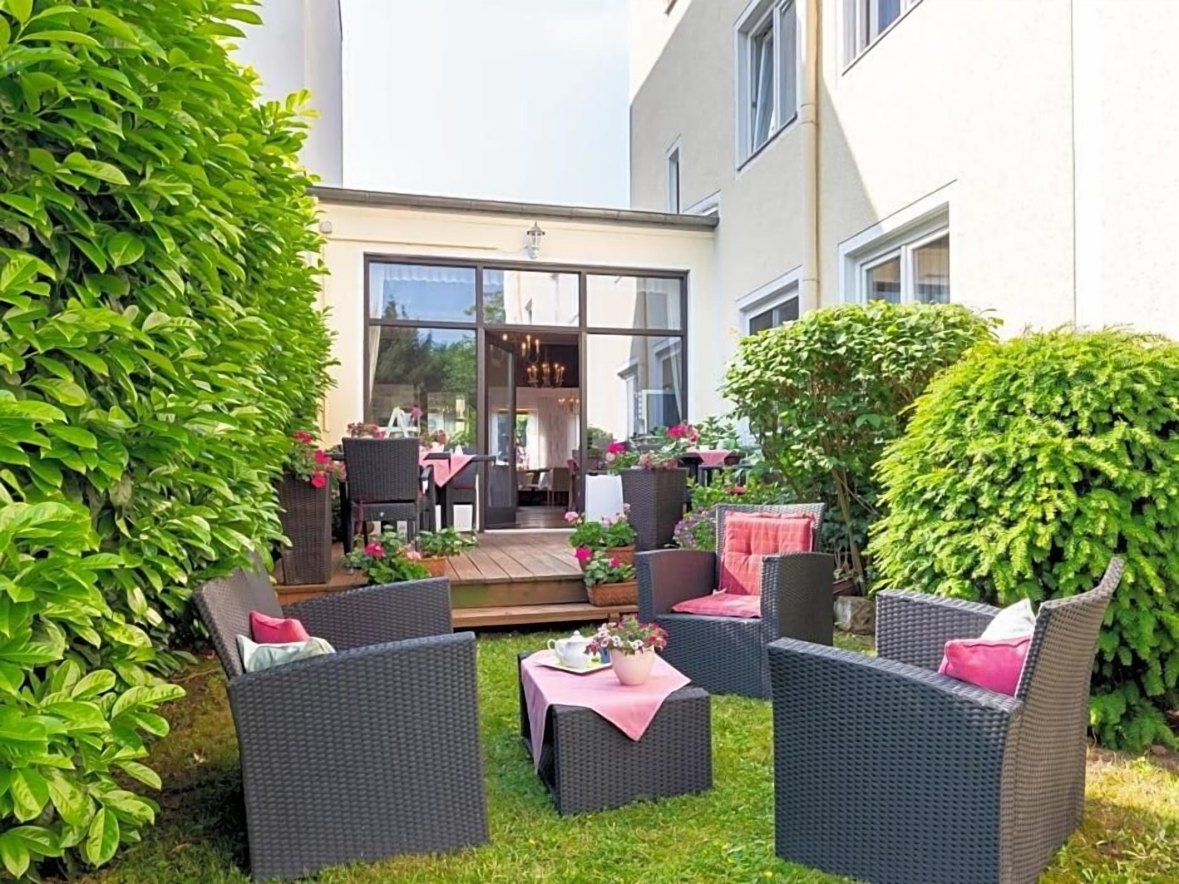 Eine Terrasse mit Korbmöbeln, ein Holzdeck und ein Gebäude mit großen Fenstern.