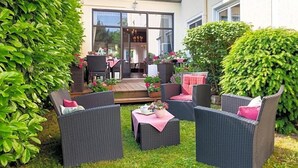 En terrasse med fletningsmøbler, træterrasse og en bygning med store vinduer.