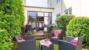 Eine Terrasse mit Korbmöbeln, ein Holzdeck und ein Gebäude mit großen Fenstern.