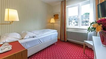 Ein Hotelzimmer mit Bett, Schreibtisch, Lampe, Heizkörper und einem Fenster mit Vorhängen.