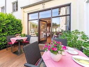 Terrassa exterior amb cadires de vimetlina i una taula preparada per dinar, un gran finestral amb vista cap a l'edifici, i plantes en testos.