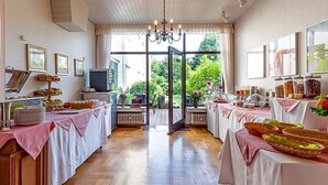 Et værelse med trægulv, en lysekrone, et buffetbord med mad og et stort vindue med udsigt til grøn vegetation.
