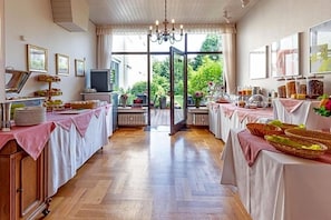 Habitació amb terra de fusta, un penjallum, una taula de buffet plena d'aliments i una finestra gran amb vista a vegetació.