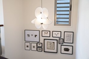 Ein Flur mit einer modernen Leuchte und einer Reihe gerahmter Kunstwerke an der Wand.
