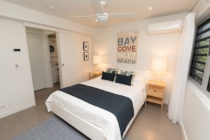 Ein Schlafzimmer mit Bett, Nachttischen, Deckenventilator, Klimaanlage, Fenster mit Vorhängen und einer Wand mit einem Schild im Strandhaus-Stil.