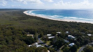 Luftaufnahme einer Küstenregion mit Strand, dichtem Wald und Wohnhäusern.