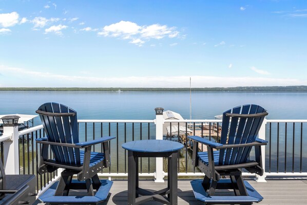 Eine Terrasse mit zwei Adirondack-Stühlen und einem kleinen Tisch mit Blick auf einen ruhigen See.