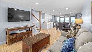En moderne stue med et fladskærms-tv, træmøbler, en sofa og udsigt til køkken og spiseområde.
