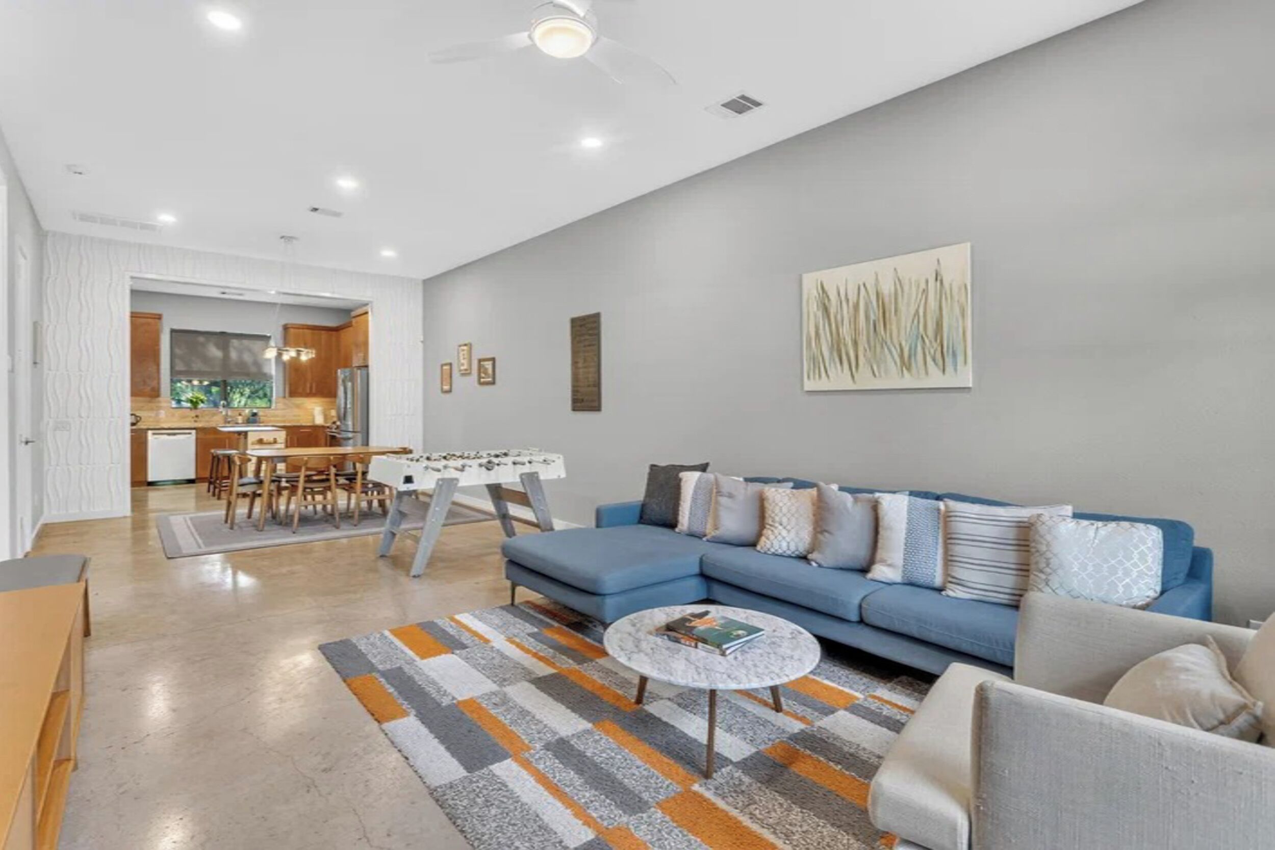Una sala de estar moderna con un sofá azul, una mesa de centro y un comedor con una mesa y sillas.