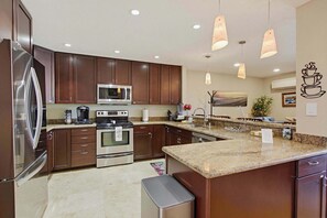 Eine moderne Küche mit Edelstahlgeräten, Holzschränken, Granit Arbeitsplatten und Pendelleuchten.