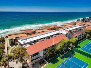 Ein Hotel an der Küste mit mehreren Stockwerken, Außenbestuhlung und Tennisplätzen.