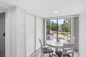 Une pièce avec une grande fenêtre, une table ronde entourée de chaises et une porte.