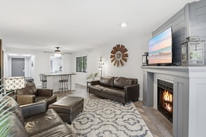A modern living room with a fireplace, a television, and a dining area. - The Lake Effect - Multiple Pools & Central Location! (Lake Ozark)