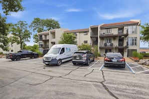 A parking lot with three cars and a white van parked in front of a residential building with balconies. - The Lake Effect - Multiple Pools & Central Location! (Lake Ozark)