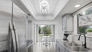 Een moderne keuken met roestvrijstalen apparatuur, een eethoek met een tafel en stoelen, en uitzicht op de omgeving.