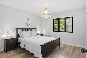 A bedroom with a bed, nightstands, a hanging light fixture, a window with a view, and a wall-mounted anchor decoration. - The Lake Effect - Multiple Pools & Central Location! (Lake Ozark)