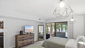 Een slaapkamer met een televisie, een houten dressoir, een bed en uitzicht door een glazen deur.
