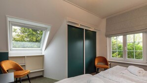 Una camera d'albergo con un letto, due sedie, una scrivania e una finestra vista alberi.