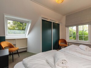 Ein Hotelzimmer mit einem Bett, zwei Stühlen, einem Schreibtisch und einem Fenster mit Blick auf Bäume.