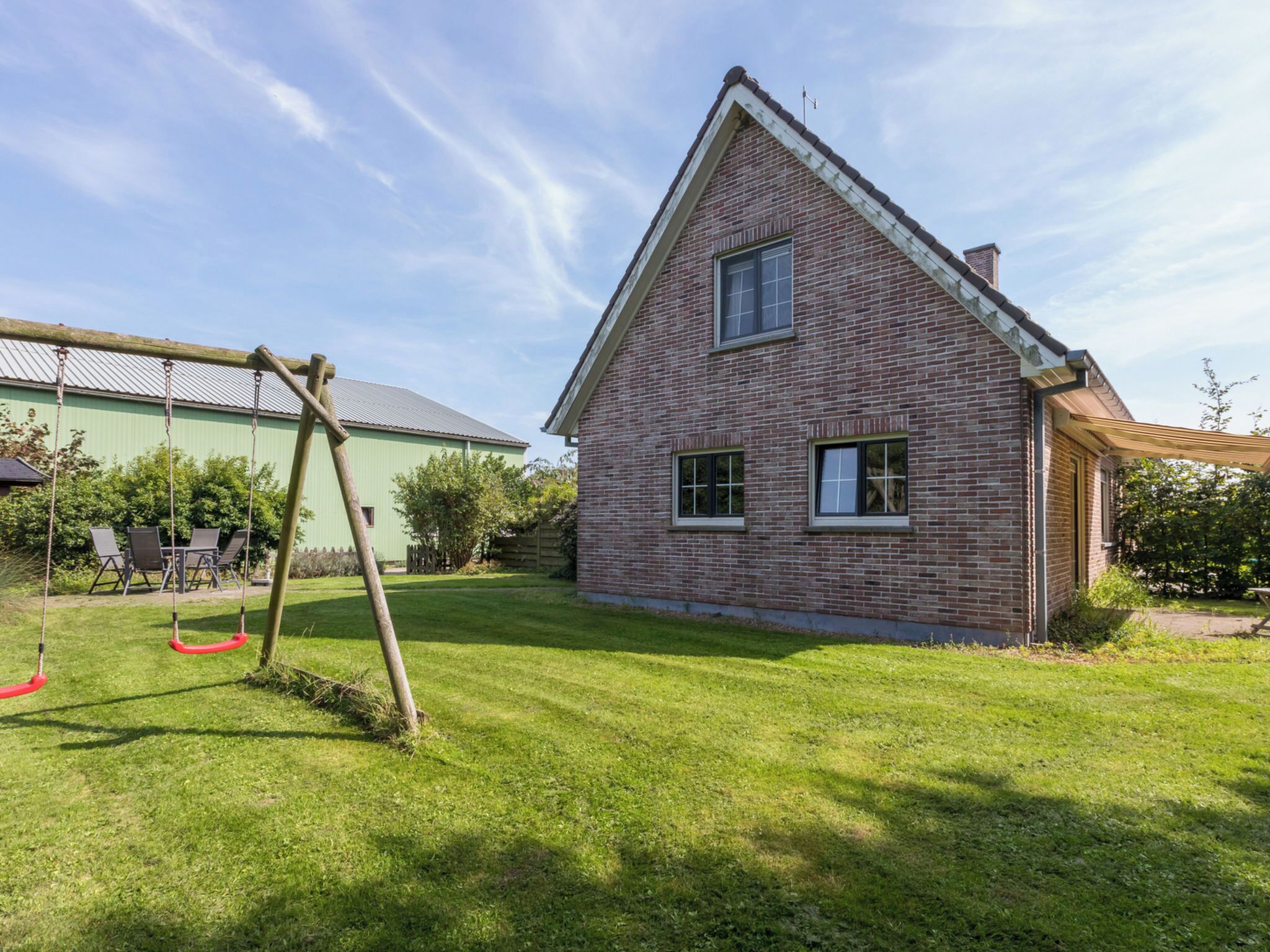 Een bakstenen huis met een schuin dak, een schommel en een groen gazon.