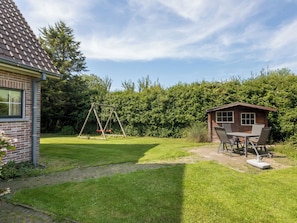 Ein Garten mit Schaukel, einer kleinen Holzhütte und einem Ziegelhaus.