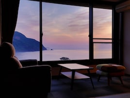 Una habitación con un amplio ventanal que da a una masa de agua y una tierra distante, un sofá, una mesita y un reposapiés.