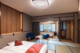 Habitación de hotel con cama, dos sillas, una mesita, un sofá, vistas a la montaña y una zona de cocina.