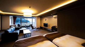 A hotel room with a large bed, a sofa, a desk with a TV, and a balcony with a view.