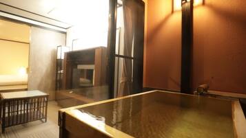 A hot spring bath area with a wooden bench, a glass partition, and a wall-mounted light fixture.