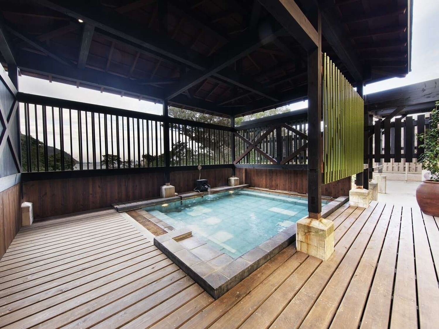 Piscina cubierta al aire libre con solárium de madera, valla de bambú y vistas al paisaje circundante.