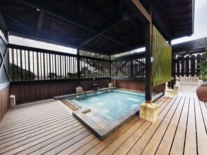 A covered outdoor swimming pool with wooden decking, a bamboo fence, and a view of the surrounding landscape. - Inatori Akao Hotel (Higashiizu)