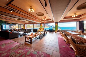 A spacious indoor area with a view of the sea, furnished with tables and chairs, and a central decorative table. - Inatori Akao Hotel (Higashiizu)