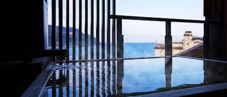A room with a large window, a wooden bench, and a view of the sea and buildings.