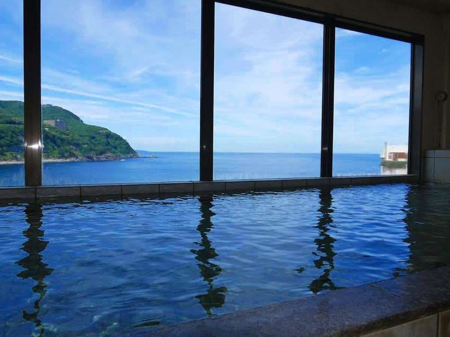 Una piscina con vistas al mar y una ladera verde.