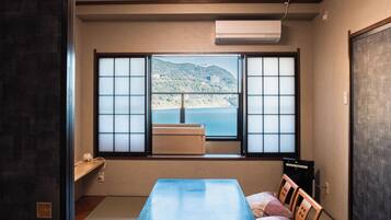 A room with a large window, a table, a chair, and a bed.