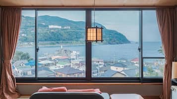 A room with a large window, a bed, a small table, and a hanging lamp.
