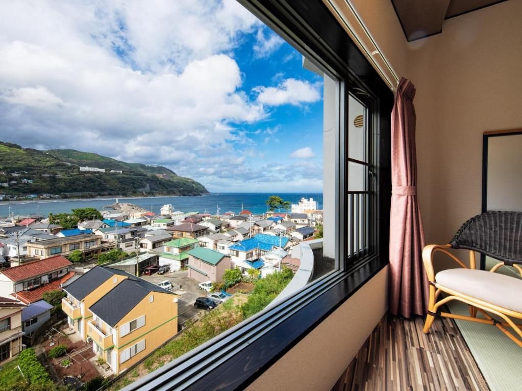 A room with a view of a coastal town, a window with curtains, and a chair.