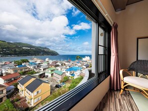 Una habitación con vistas a un pueblo costero, una ventana con cortinas y un sillón.